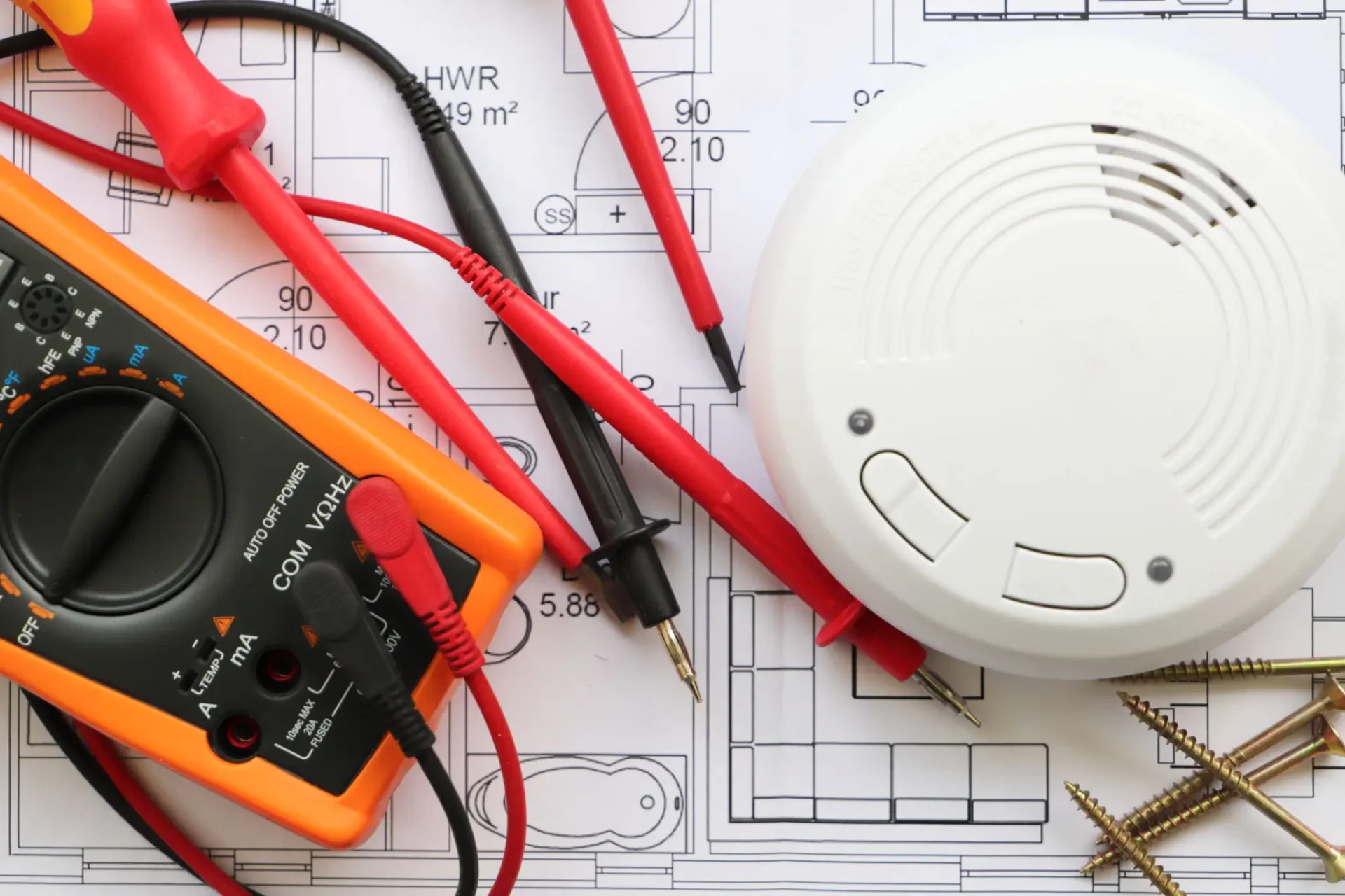 Electrical testing tools and smoke detector on building plans.